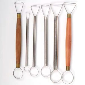 Peut inclure: Un ensemble de six outils de poterie en forme de boucle. Les outils ont des boucles et des tiges en acier inoxydable. Deux outils ont des manches en bois, tandis que les autres ont des manches en métal. Les boucles sont de formes et de tailles variées, adaptées à la sculpture et au modelage de l'argile.