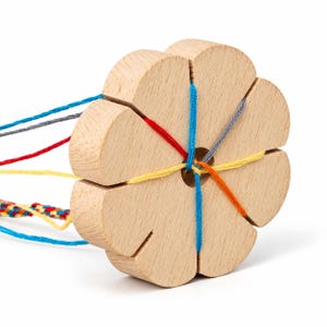 May include: A round, light-colored wooden kumihimo braiding disk with eight evenly spaced notches along the edge and a center hole. Several strands of colorful yarn, including blue, red, yellow, orange, and gray, are threaded through the notches.