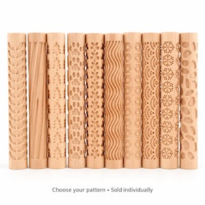 Puede incluir: Una colección de diez rodillos cilíndricos de madera, cada uno con un patrón en relieve distinto que incluye hojas, líneas diagonales, árboles, huellas, flores, ondas, círculos, escamas, copos de nieve y formas orgánicas. El texto dice: Choose your pattern • Sold individually.