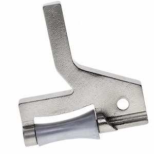 May include: A silver-toned metal sewing machine presser foot attachment featuring a textured finish on the upper arm, a circular mounting hole, and a smooth, light gray cylindrical roller component positioned at the base for fabric guidance.