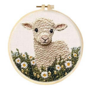 May include: Embroidered artwork of a lamb in a field of daisies, set in a wooden embroidery hoop. The lamb is beige with black eyes and a pink nose. The daisies have white petals and yellow centers.