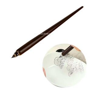May include: A dark brown calligraphy pen with a pointed nib. The pen is shown in use, creating a black ink design on a white surface. The pen has a long, tapered wooden handle.