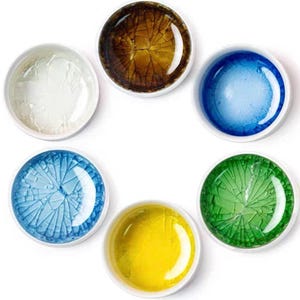 May include: Six small, round, white-rimmed bowls with colorful, textured interiors. The colors include white, brown, blue, light blue, yellow, and green. The bowls have a cracked glass appearance.