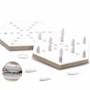 May include: Two hexagonal white game boards with multiple circular indentations and several white conical game pieces. Some pieces are placed upright in the holes, while others are scattered around the boards. A small circular inset shows a piece.