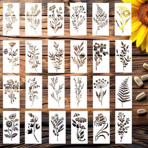 Peut inclure: Un ensemble de vingt-quatre pochoirs rectangulaires blancs présentant diverses illustrations botaniques, notamment des fleurs, des feuilles, des fougères et des brindilles. Chaque pochoir affiche une silhouette noire ou brune unique.