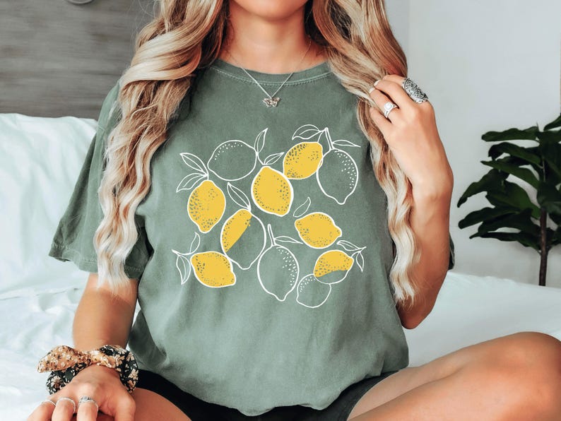 a woman sitting on a bed wearing a t - shirt with lemons on it