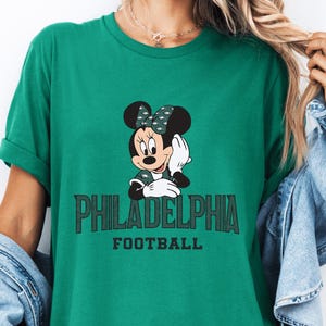 A green t-shirt with a Minnie Mouse graphic and the text "PHILADELPHIA FOOTBALL" printed on it.