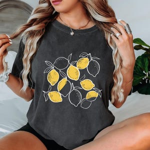 a woman sitting on a bed with a black shirt with lemons on it