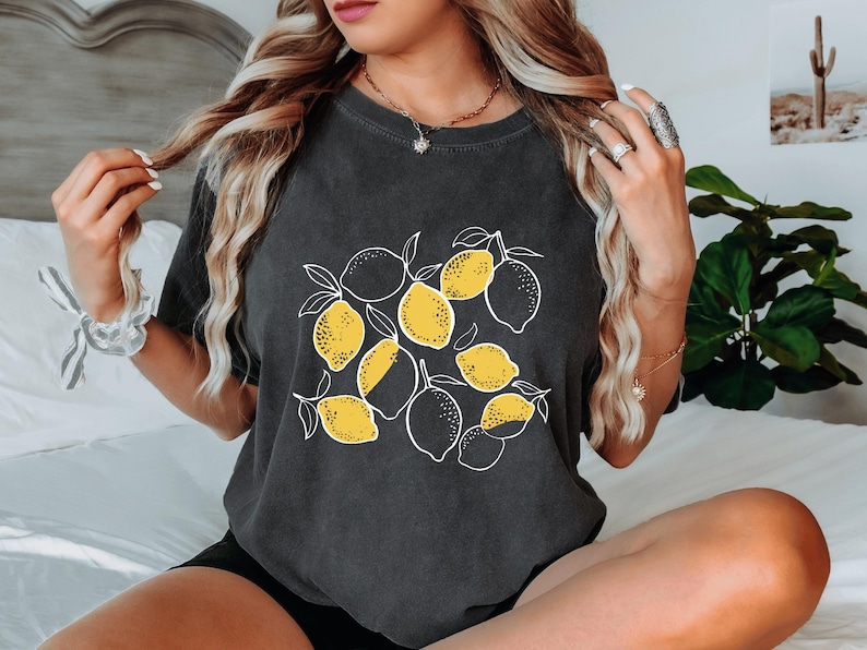 a woman sitting on a bed with a black shirt with lemons on it
