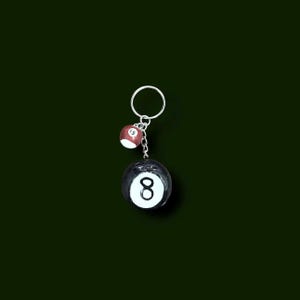 May include: A keychain featuring two billiard balls. The larger ball is black with a white number 8. The smaller ball is red with the number 15. Both balls are attached to a silver-colored key ring.