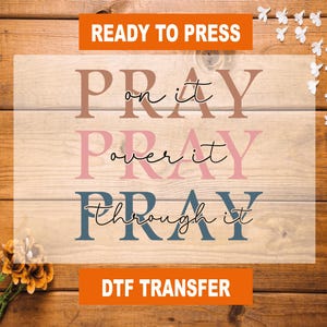May include: Ready to press iron-on transfer design with the text "Pray on it, Pray over it, Pray through it" in brown, pink, and blue lettering on a wood background. DTF Transfer.