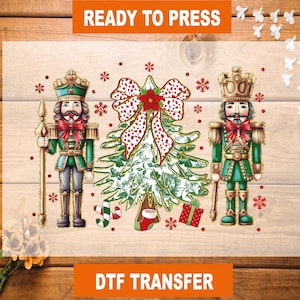 May include: A digital design featuring two nutcracker soldiers flanking a Christmas tree with a red and white bow. The design is ready to press and is a DTF transfer.