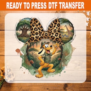 May include: A Ready to Press DTF transfer featuring a cartoon dog in a safari outfit with a leopard print bow. The design includes circular scenes of a tree and a giraffe with zebras, all set against a watercolor-style background with greenery.