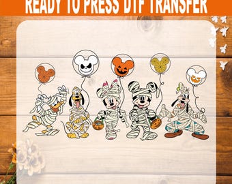 May include: A ready to press DTF transfer featuring five cartoon characters wrapped in white bandages like mummies, each holding a string attached to a circular balloon with a unique Halloween-themed design, including jack-o'-lanterns and spider webs.