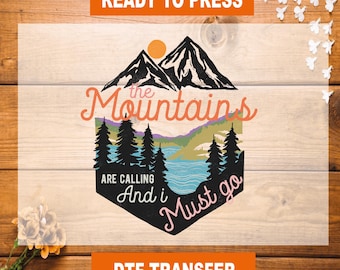 Könnte beinhalten: Ein DTF-Transfer mit einem Berg- und See-Design. Der Text "the Mountains are calling and I must go" ist in einer dekorativen Schriftart dargestellt. Das Bild enthält eine Sonne, Bäume und Berge.