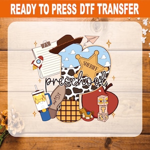 May include: A Ready to Press DTF transfer featuring a heart-shaped design with a cow print and blue sky pattern. It includes a brown cowboy hat, a sheriff badge, a clipboard, a tumbler, a boot labeled Andy, a red apple, and blocks with the word preschool.