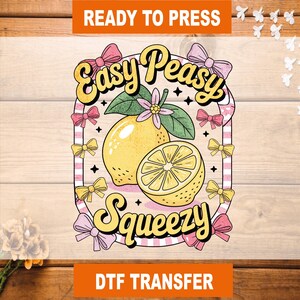 May include: A DTF transfer with a lemon design. The design features a whole lemon and a lemon slice, with the words "Easy Peasy Squeezy" in a retro font. Pink and yellow bows surround the lemon illustration. The words "Ready to Press" and "DTF Transfer" are also included.