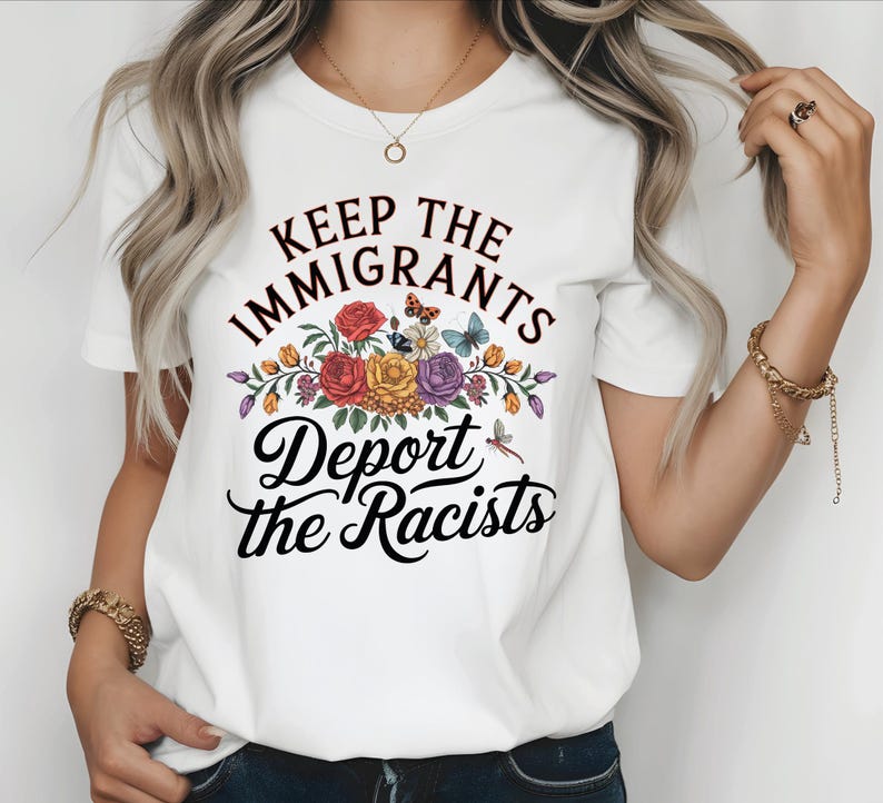 May include: White t-shirt featuring the text "Keep the Immigrants, Deport the Racists" in black script. The design includes a floral arrangement with red, yellow, and purple flowers, butterflies, and a dragonfly.