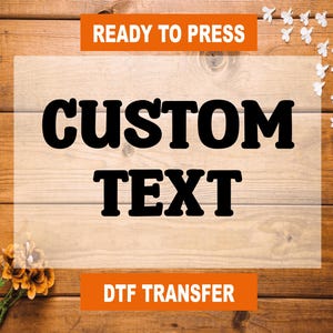 May include: Ready to press custom text DTF transfer on a wood background with white flowers.