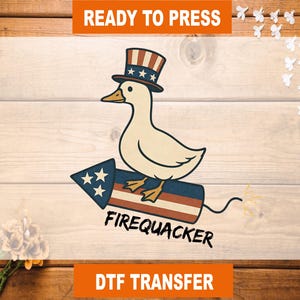 May include: A cartoon duck wearing a patriotic top hat, riding a firework with the text "FIREQUACKER." The design includes red, white, and blue colors, and the words "READY TO PRESS" and "DTF TRANSFER" are also present.