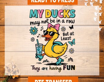 May include: A DTF transfer design featuring a yellow duck wearing sunglasses, a pink bow, and roller skates, holding a drink. The text reads "MY DUCKS may not be in a row But at Least They are having FUN."