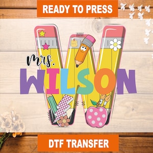 May include: A colorful DTF transfer featuring the name "Mrs. Wilson" in a large, stylized "W" shape. The design incorporates pencil-themed elements, including a cartoon pencil, a flower, and an apple. The words "READY TO PRESS" and "DTF TRANSFER" are also present.