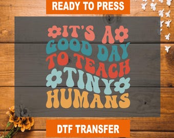 May include: Ready to press iron-on transfer design with the text "It's a good day to teach tiny humans" in a retro font with colorful flowers. DTF transfer.