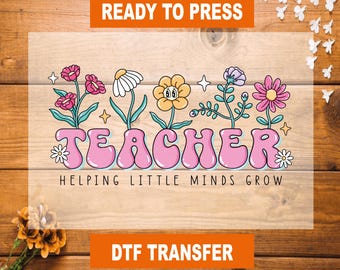 May include: A pink and white iron-on transfer design with the word "TEACHER" in large, bubble letters surrounded by colorful flowers. The text "Helping Little Minds Grow" is below the word "TEACHER".