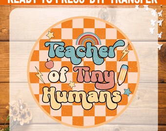 May include: Round DTF transfer with the text "Teacher of Tiny Humans" in a retro font. The design includes a rainbow, apple, pencil, stars, and lightning bolts, set against an orange and white checkered background.