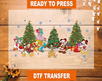 Puede incluir: Transferencia DTF con personajes de Disney en una escena navideña. El diseño incluye árboles de Navidad decorados, copos de nieve y personajes como Mickey y Minnie Mouse, Donald Duck y Pluto. Se muestra el texto "READY TO PRESS" y "DTF TRANSFER".