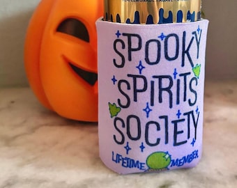 May include: A gold can of Liquid Death Dead Billionaire tea lemonade with a purple can cooler that says "Spooky Spirits Society Lifetime Member".
