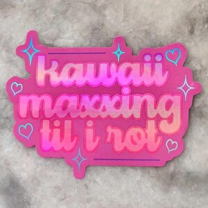 May include: A pink sticker with the words "Kawaii maxxing til i rot" in a bubble font. The sticker has a holographic effect and is decorated with hearts and stars.