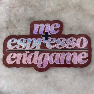 Puede incluir: Una pegatina con las palabras "me + espresso endgame" en una fuente brillante, morada y plateada. La pegatina tiene un borde marrón rojizo oscuro y una línea negra que separa "espresso" y "endgame".