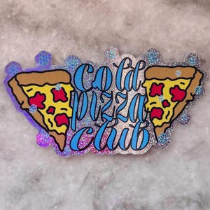 May include: A glittery sticker featuring the words "Cold Pizza Club" in blue script. Two cartoon pizza slices with yellow crusts, red toppings, and brown crusts are on either side of the text. The sticker has a silver glitter border.