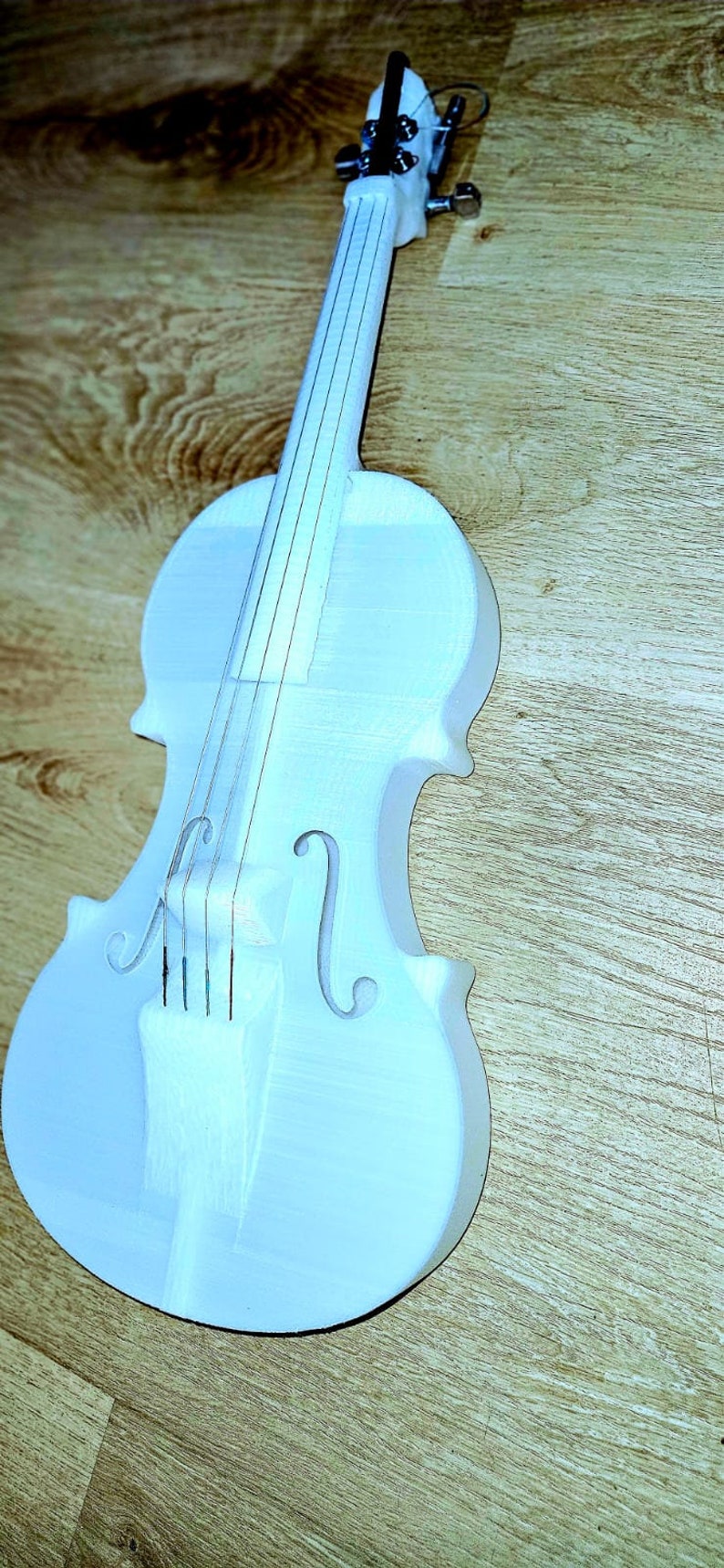 May include: A white painted wooden violin with a simple design. The violin has four strings and a wooden neck.