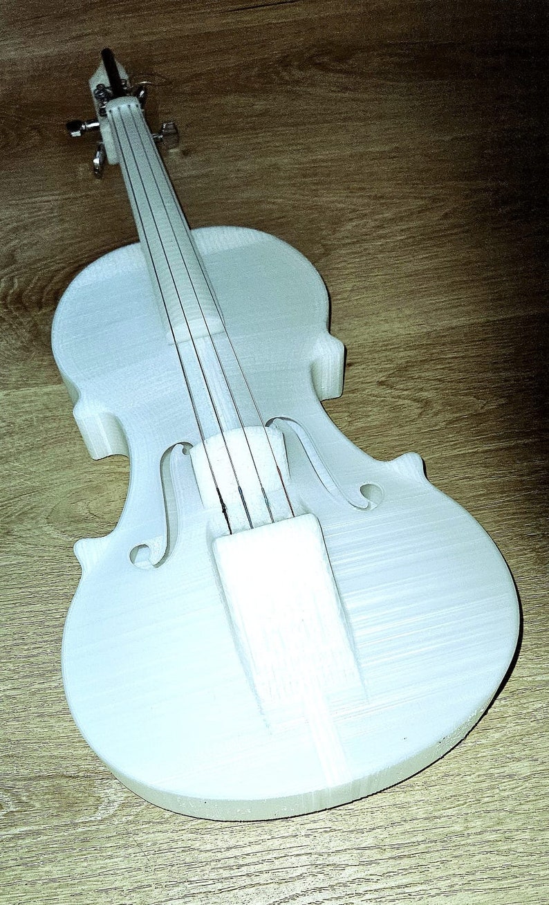 May include: A white 3D printed violin with strings, set against a wooden background.