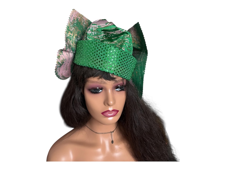 May include: A green sequined head wrap with a matching bow and a pink and green patterned accent. The head wrap is worn on a mannequin with long, dark hair and a necklace.