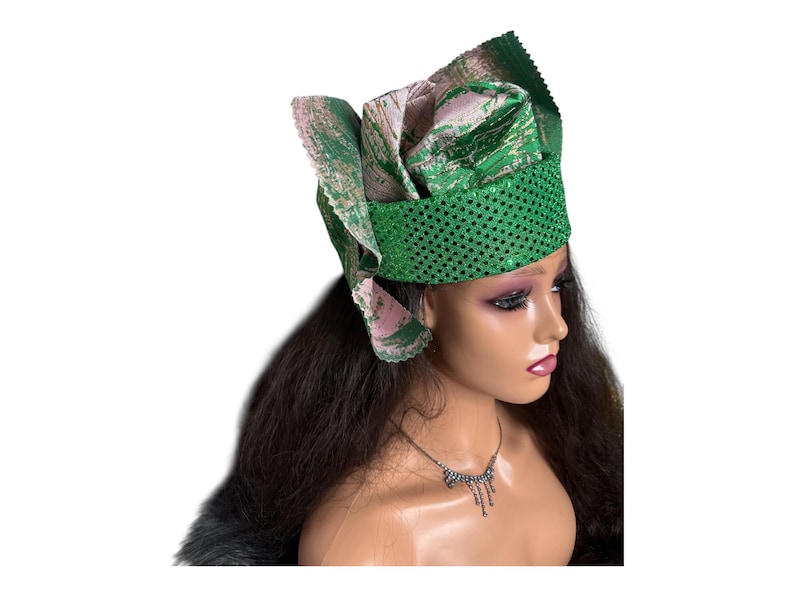 May include: A green and pink head wrap with a sequined band. The head wrap has a layered design with a floral pattern. The mannequin is wearing a silver necklace. The head wrap is a fashion accessory.