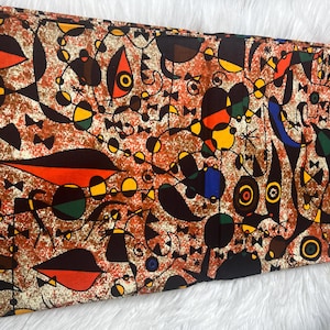 May include: A colorful fabric with a geometric pattern in shades of red, orange, yellow, green, blue, and black. The fabric has a white background with a brown speckled texture. The fabric has the text "CK PRINTS BOGOLAN * NT 8500" printed on the left side.