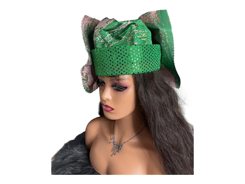 May include: A green and pink head wrap with a sequined band. The head wrap has a patterned design and is worn on a mannequin. The mannequin has long dark hair and a silver necklace.