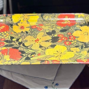 Peut inclure: Un plateau de service en métal jaune, orange et vert avec un motif floral. Le plateau a deux pieds métalliques de chaque côté.