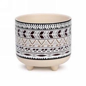 May include: A white ceramic planter with a geometric pattern in black and brown. The planter has three short legs and is ideal for small plants.