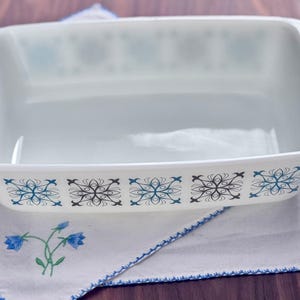 May include: White ceramic baking dish with a blue and black geometric pattern. The dish is empty and sitting on a white cloth.