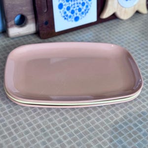 May include: Two pink rectangular ceramic serving platters with a yellow rim. The platters are stacked on top of each other.