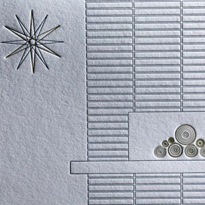 May include: A textured, light gray card with an embossed design. The design includes a starburst, rectangular blocks, and a series of concentric circles. The overall aesthetic is minimalist and geometric.
