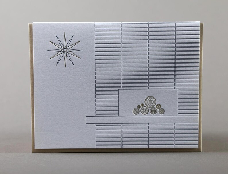 May include: A greeting card with a minimalist design. The card features a starburst graphic on the left and a fireplace illustration on the right. The fireplace design includes a series of horizontal lines and circular shapes. The card has a neutral color palette.