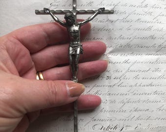 May include: A detailed silver crucifix featuring a figure of Jesus with outstretched arms. The cross has a simple design, and the figure is intricately detailed. The background is an aged document with handwritten text.