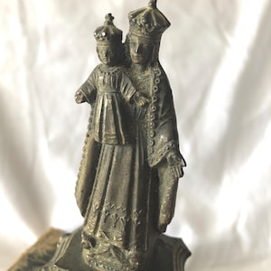 Op de afbeelding: Een bronzen beeld van een gekroonde vrouw die een kind vasthoudt dat ook een kroon draagt. De figuren dragen sierlijke gewaden. Het beeld is gemonteerd op een decoratieve basis.