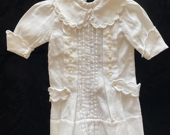 May include: A white ribbed knit shirt featuring a scalloped collar, short sleeves with scalloped cuffs, and two vertical rows of small buttons down the front. The garment includes two decorative scalloped pocket flaps at the waist, each with a single button.