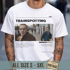 May include: White t-shirt featuring the movie title "Trainspotting" with a movie still. The shirt includes the year "1996" and the text "ALL SIZE S - 5XL VINTAGE".